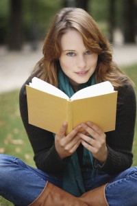 Beautiful young brunette with blue eyes reading a book,sitting in a park